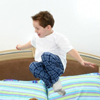 Five year old boy in pajamas jumping in bed.