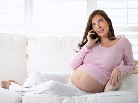 Mother about to start a family resting on a white sofa and using a phone