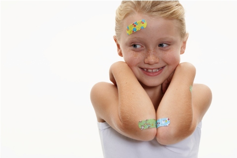 Girl (7-9) with plasters on head and arms, smiling