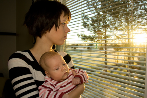 Young mother looking out from the window with her baby